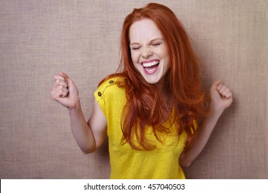 Single gorgeous young red haired woman in yellow shirt dancing or rejoicing about something over simple brown cloth background with copy space