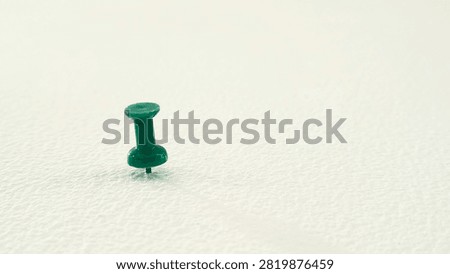 Single Green Push Pin Plastic Thumb Tack Stuck on White Textured Surface with Copy Space