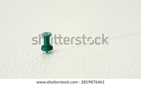 Single Green Push Pin Plastic Thumb Tack Stuck on White Textured Surface with Copy Space