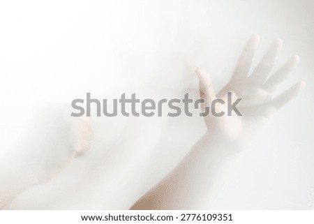 A single hand presses against a translucent white surface with spread fingers creating an obscure shadowy silhouette. The slow motion blur gives the arm a mysterious ethereal appearance.