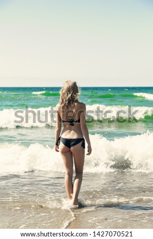 single happy young woman in swimsuit walking at sea surf with splashes