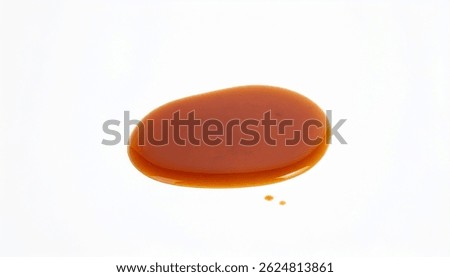 A single, irregular puddle of glossy amber caramel sauce rests on a stark white background. Two tiny satellite droplets accompany it, suggesting recent spillage.