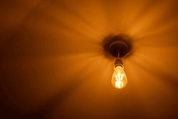 Single Isolated Incandescent Filament Light Bulb Sending Out A Warm Glow Against A White Ceiling
