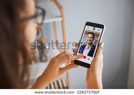 Single lady looking for boyfriend on online dating app or website. Young woman holding mobile phone, looking at profiles of male candidates and giving like to photo of handsome businessman. Crop shot