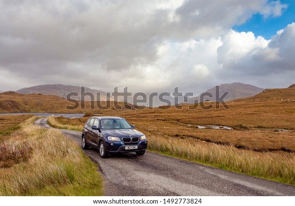 Single lane\
road, Scotland, UK - April 10, 2019: car driving on the narrow one\
lane road in rural Scottish\
Highlands