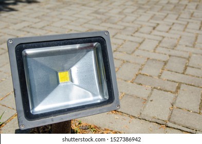 Single Led Lamp Fixed On A City Sidewalk. Outdoor Lightning Equipment Mounted On Ground. One Floodlight Led Lamp On Paved Street Walkways