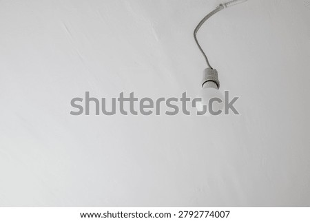 Single light bulb hanging from a wire on a white ceiling in a minimal interior setting