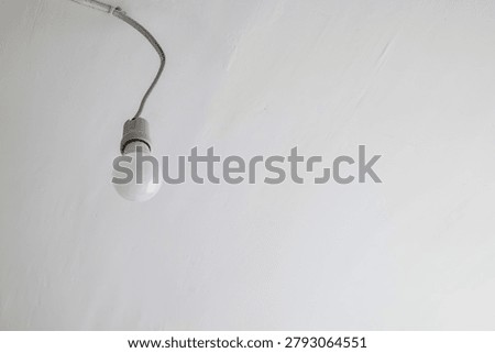 Single light bulb hanging from a wire on a white ceiling in a minimal interior setting