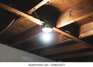 A Single Light On The Ceiling In A Dark Unfinished Basement.