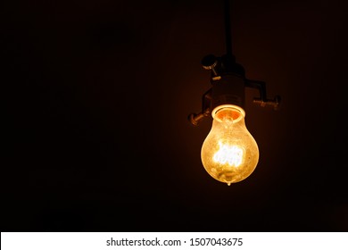 Single Lightbulb Hanging From A Wire In A Dark Room With A Warm Glow