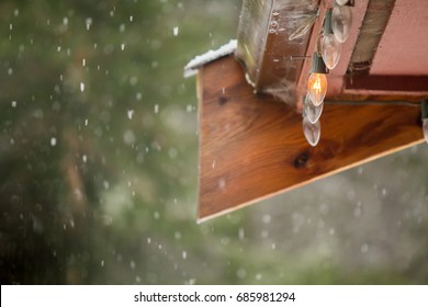 Single Lit Bulb In A String Of Old Fashioned Christmas  Lights Strung Along A Wooden Eve On A Snowy Afternoon 