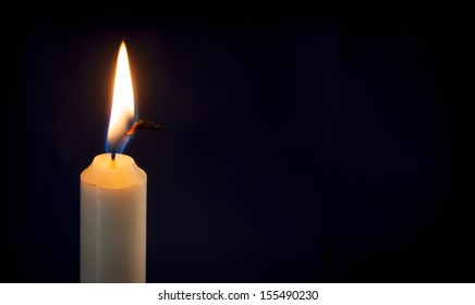 A Single Lit Candle On A Dark Background.