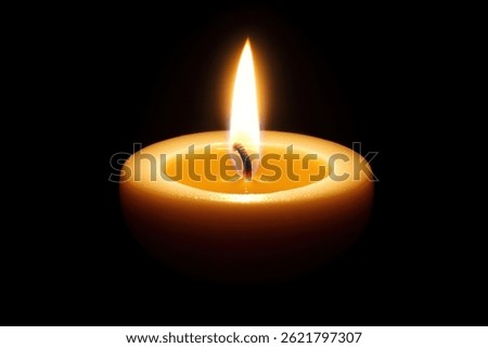 A single, lit candle sits in the center of a black background its warm yellow flame casting a soft glow.