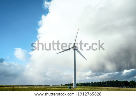 Single lone electric generating wind turbine windmill with dramatic big storm cloud and rainbow and nature park forest woodland behind on bright day
