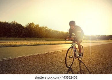 Single Male Bicyclist Wearing Shorts, Helmet And Sunglasses Training For Long Distance Racing On Road Bike At Sunrise With Copy Space In Front