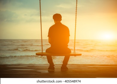 Single Man Alone While Swinging On The Beach At Sunset