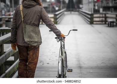 A Single Man Dressed In Old Clothes On The Embankment With The Bike