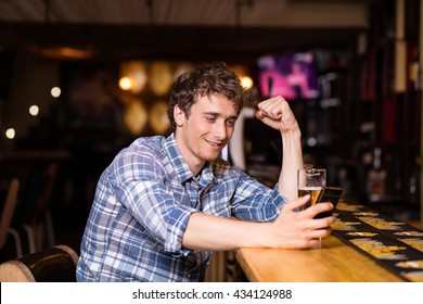 Single Man Drinking Beer At Bar Or Pub, Using His Cellphone, Texting Or Betting