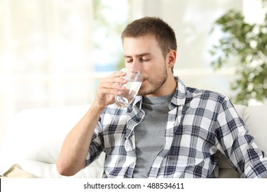 Single man drinking water from a glass sitting on a couch at home