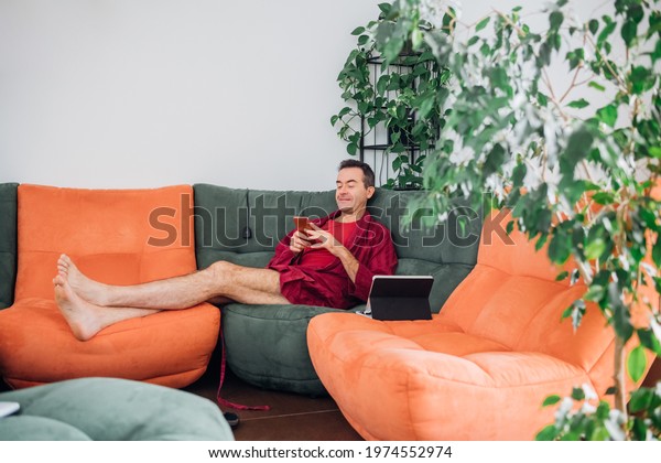 Single man indoor at home relaxing on sofa, using\
smartphone and tablet