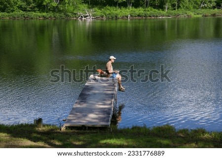 a single man sits on the edge of a dock on a lake while fishing on a sunny day