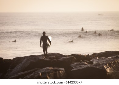 Single Man With Surf Standing At The Anchor Point In Morocco Waiting For A Wave During Sunset.