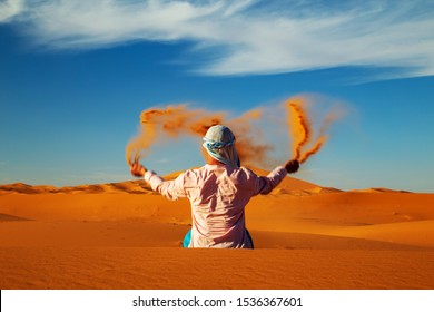 Single Man throws sand in the Sahara desert at sunset. Erg Chebbi, Merzouga,  Morocco.