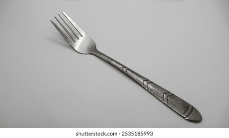 A single metal fork with a patterned handle, lying diagonally on a light surface.