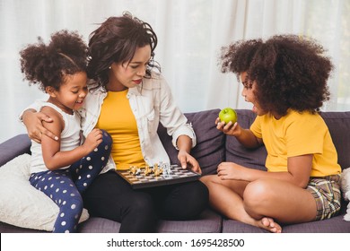 Single Mom Good Care, Teaching Her Childs To Be Genius And Clever Little Girls Learning To Play Chess Boardgame Eating Fruit For Healthy.