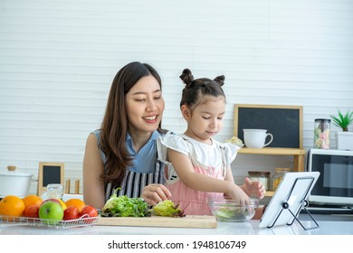 Single Mother With A Cute Baby Daughter Learn To Cook Online Through An Application Together At The Kitchen In The House 
