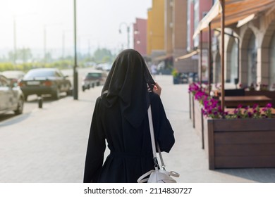 A single Muslim woman walks through empty big city rear view.