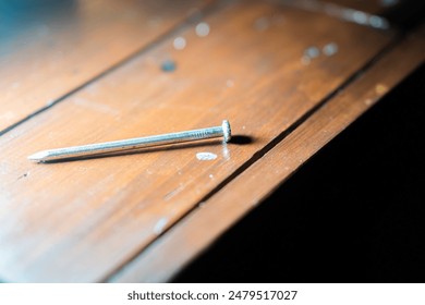 A single nail standing upright on a wooden surface with a blurred background. - Powered by Shutterstock