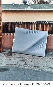 Single Old Mattress Leaning Against Brick And Wood Wall In Alleyway In Los Angeles, CA. 