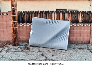 Single Old Mattress Leaning Against Brick And Wood Wall In Alleyway In Los Angeles, CA. 