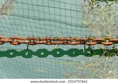 A single old rusty thick metal chain hanging on the surface of the water in the bay, A lone, ancient, corroded, hefty metal chain suspends above the water's surface in the harbour