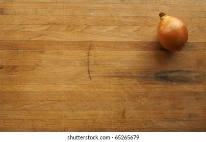 A single onion sits on a worn butcher block cutting board with suffient room for text
