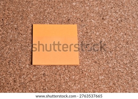 Single orange sticky note on a cork board. Colored blank note pad reminders. 