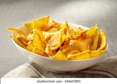 Single Oval Shaped White Bowl Of Yellow Tortilla Chips Topped With Melted Cheese Placed On Folded Fabric Napkin Over Tablecloth With Copy Space