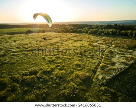 A single paraglider enjoys an exhilarating flight over expansive green fields under the clear blue sky.