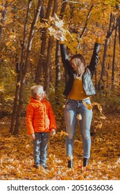 Single Parent Family Playing With Autumn Leaves In Park. Happy Mom And Son Throw Autumn Leaves Up In Fall Park.