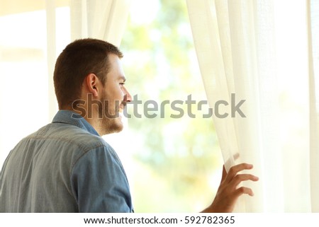 Single pensive man looking outdoors through a window at home or hotel