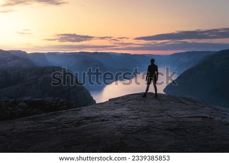 The single person standing alone on the edge of the cliff Preikestolen in Rogaland county in Norway watching the sun rising. Flat top cliff is a tourist attraction above Lysefjorden fjord. 