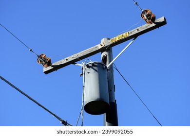 Single phase distribution transformer on the weathered wooden pole. Yellow high voltage sign.