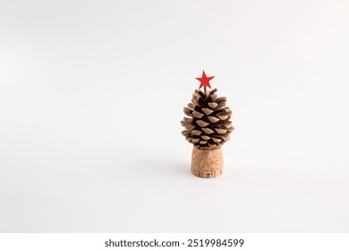 Single pine cone on a cylindrical cork base with a red star on top, white background, creative minimalist Christmas tree concept, sustainable holiday decoration, natural elements - Powered by Shutterstock