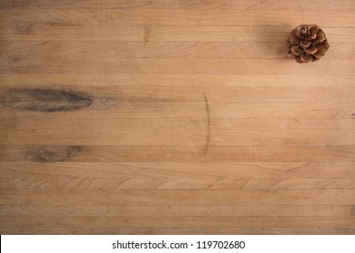 A Single Pine Cone Sits On A Worn Butcher Block Counter