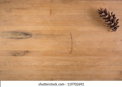 A single pine cone sits on a worn butcher block counter