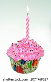 A Single Pink First Birthday Cupcake With A Lit Pink And White Striped Lit Candle.  Close Up With Copy Space.