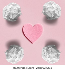 Single pink heart shape centered perfectly among four discarded white paper balls creating a minimalist artistic composition with soft shadows on a flat pastel pink background surface showcasing concepts of love rejection and creative thinking in a professional studio