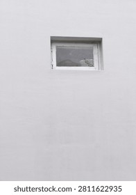 A single rectangular window with a white frame is set high on a textured white plaster wall, creating a clean minimalist composition.