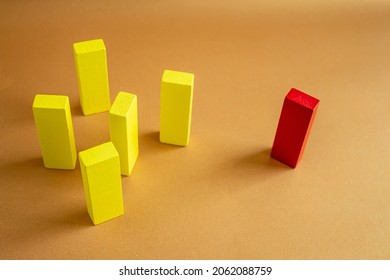 A single red block standing away from a group of yellow wooden blocks. Concept of individuality, discrimination, exclusion, loneliness.